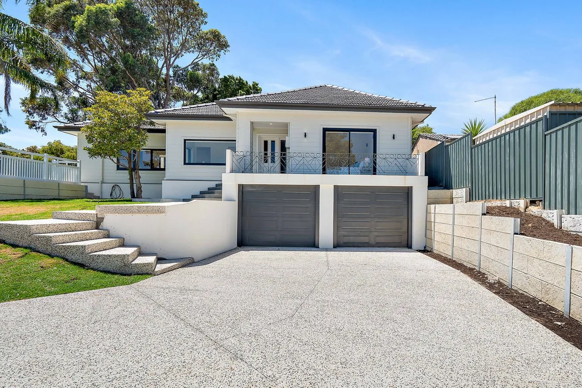 White residential facade with a tiled roof, raised terrace and two garage doors.