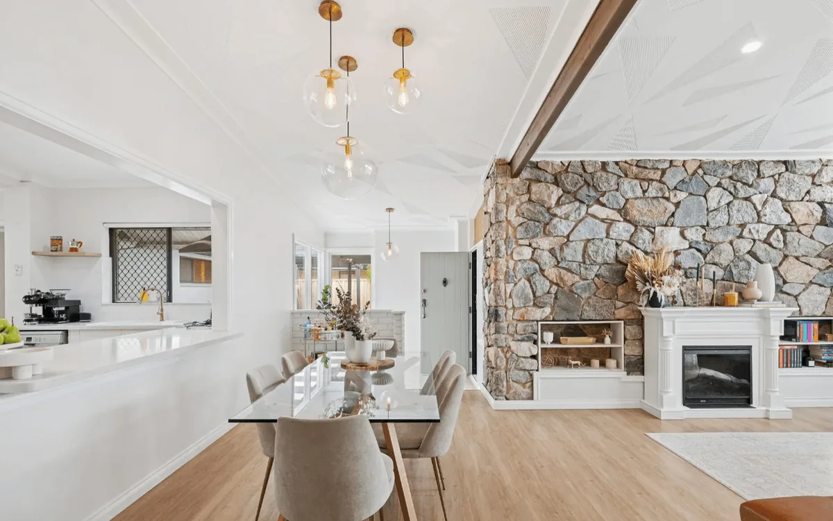 Light-filled dining and living space with a stone feature wall, timber flooring and pendant lights.