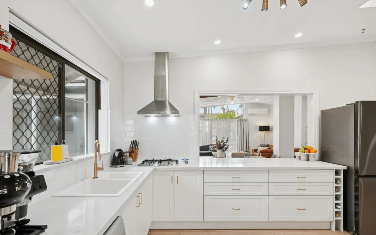 White kitchen cabinetry and a stone benchtop connecting to a dining space.